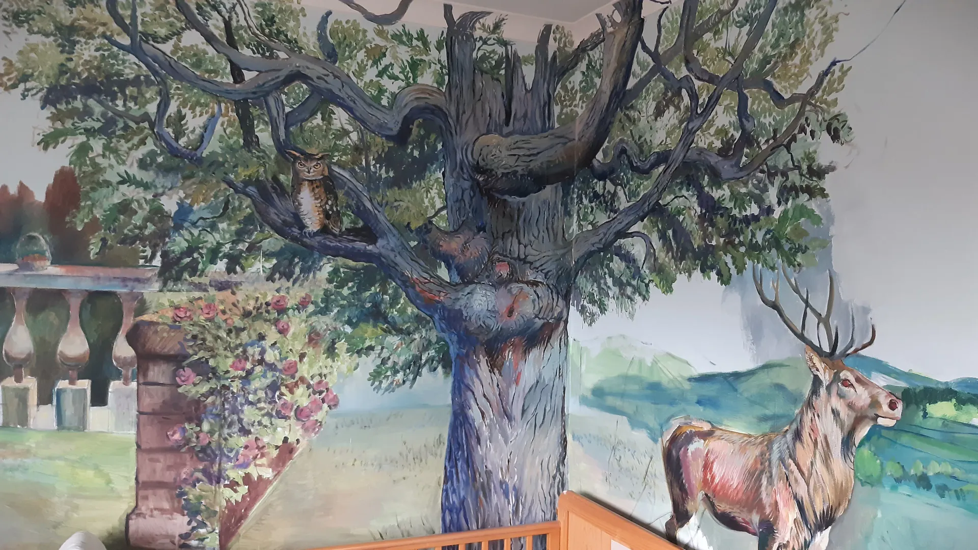 Hand-painted forest mural with a large tree, owl, and stag across a wall